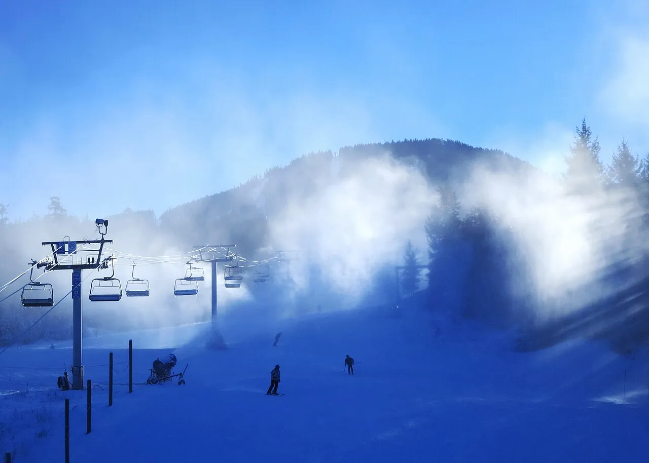 Snowmaking machines working at the base of Whistler Mountain in winter with skiers on the run below