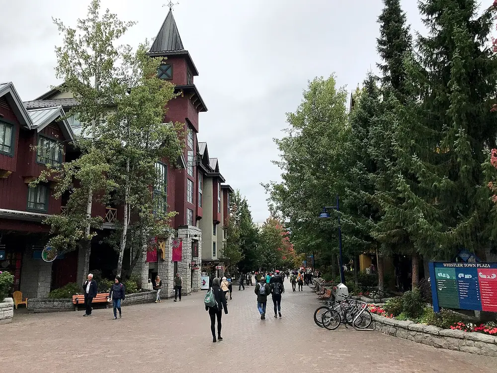 Town Plaza in Whistler Village with flower baskets, benches and pedestrians on a rainy day