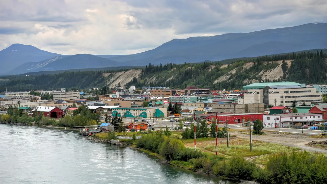 Downtown Whitehorse along the turquoise Yukon River, with clay bluffs and forested hills behind