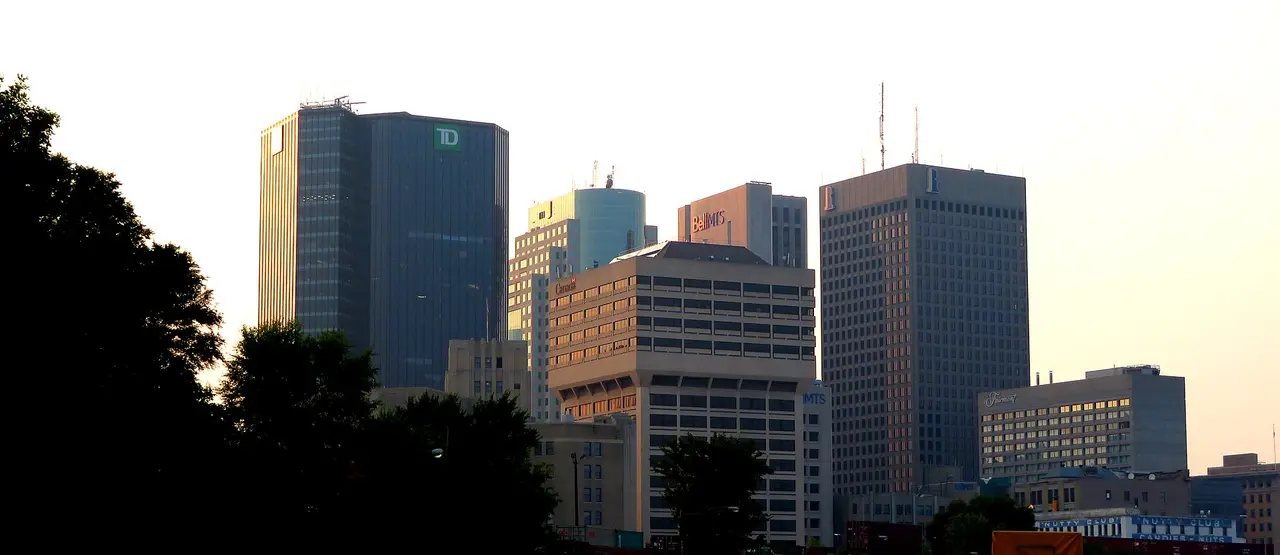 The downtown Winnipeg skyline seen across low prairie buildings under a wide sky