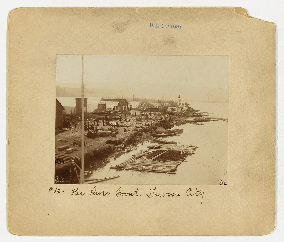 A black-and-white 1897 photograph of the Dawson City riverfront crowded with tents, boats and stampeders