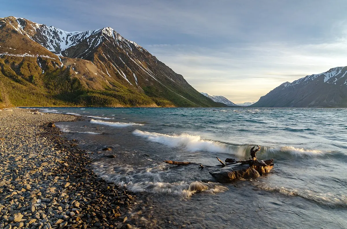 Evening light on the still water of Kathleen Lake beneath dark mountains in Kluane National Park