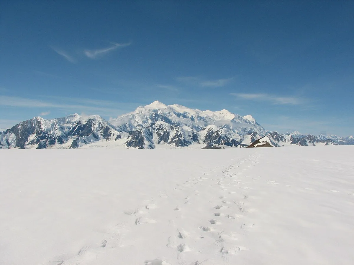 The broad snow-covered massif of Mount Logan rising from the white Kluane Icefield under a pale sky
